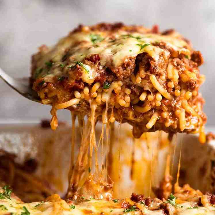 Lifting a cheesy piece of Baked Spaghetti from casserole dish