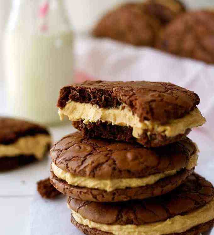 A pile of Brownie Cookie Sandwiches with Peanut butter Frosting, with milk in background