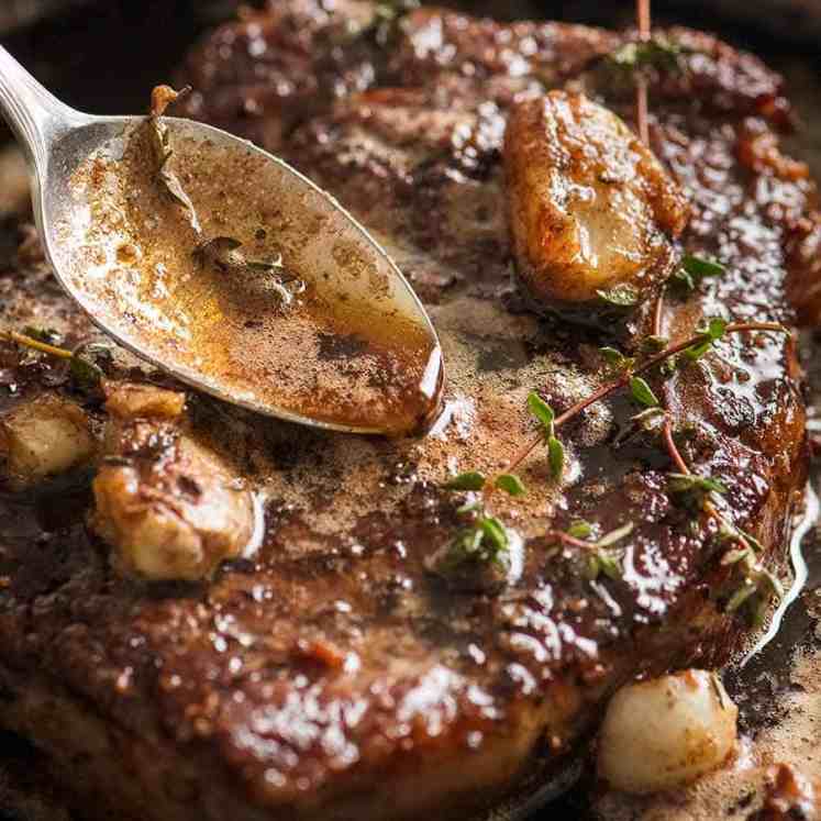 Close up of spoon drizzling browned garlic thyme butter sauce over steak