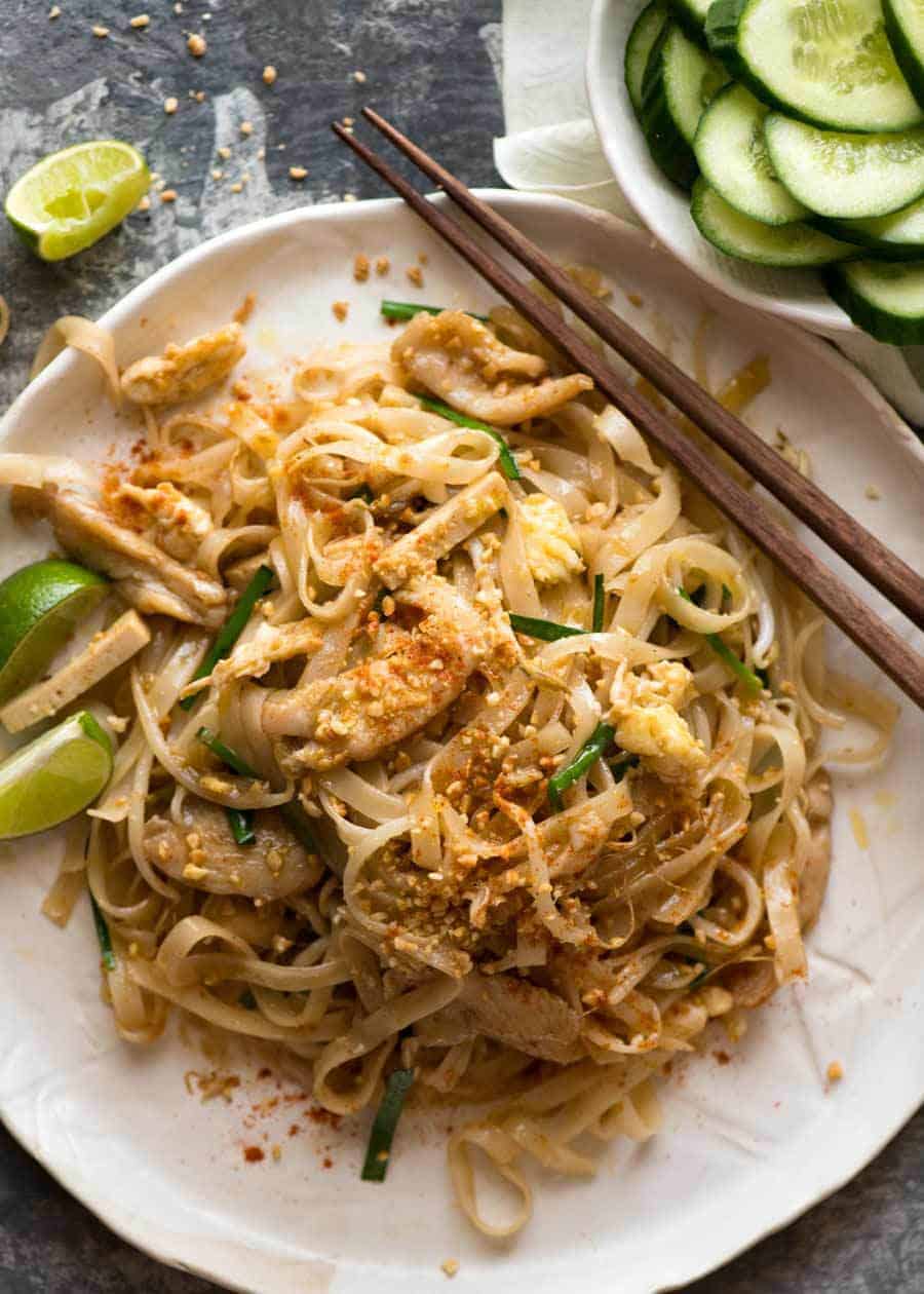 Overhead photo of Chicken Pad Thai on a rustic white plate with a side of cucumbers, ready to be eaten.