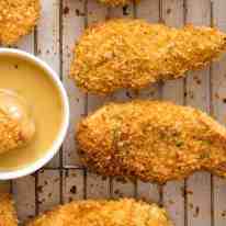 Crunchy Baked Chicken Tenders on a tray with a Honey Mustard Dipping Sauce on the side, fresh out of the oven