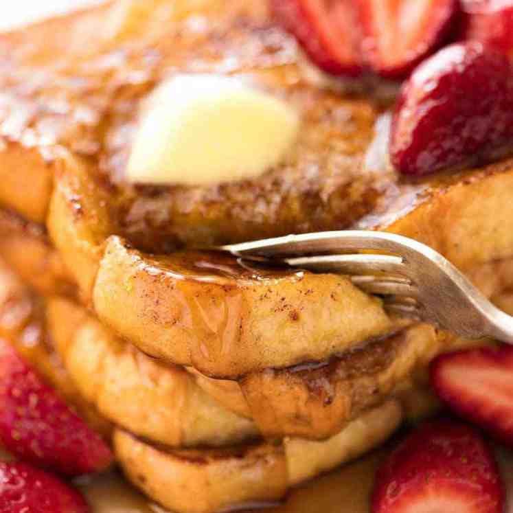 Fork cutting into a stack of French Toast smothered in maple syrup