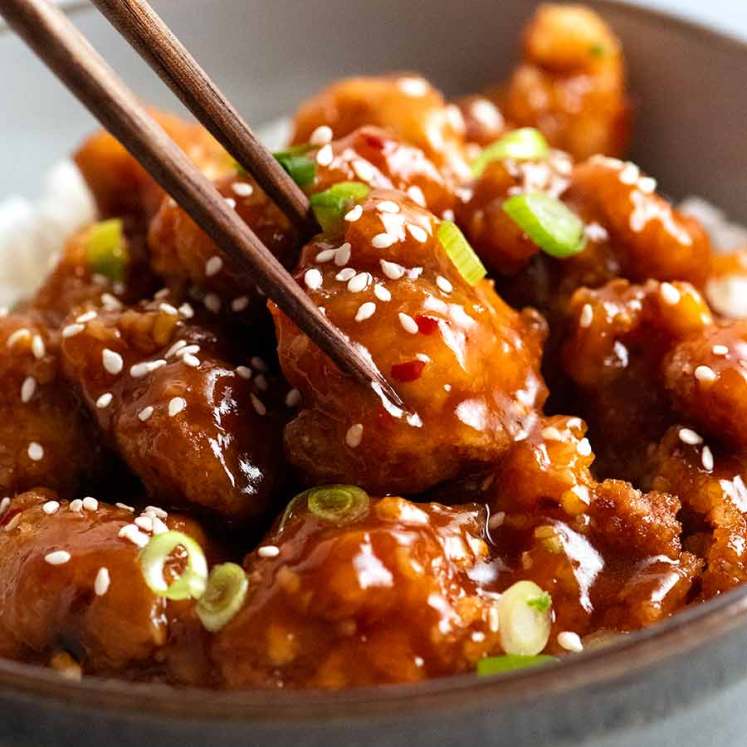 Close up of chopsticks picking up a piece of General Tso's Chicken