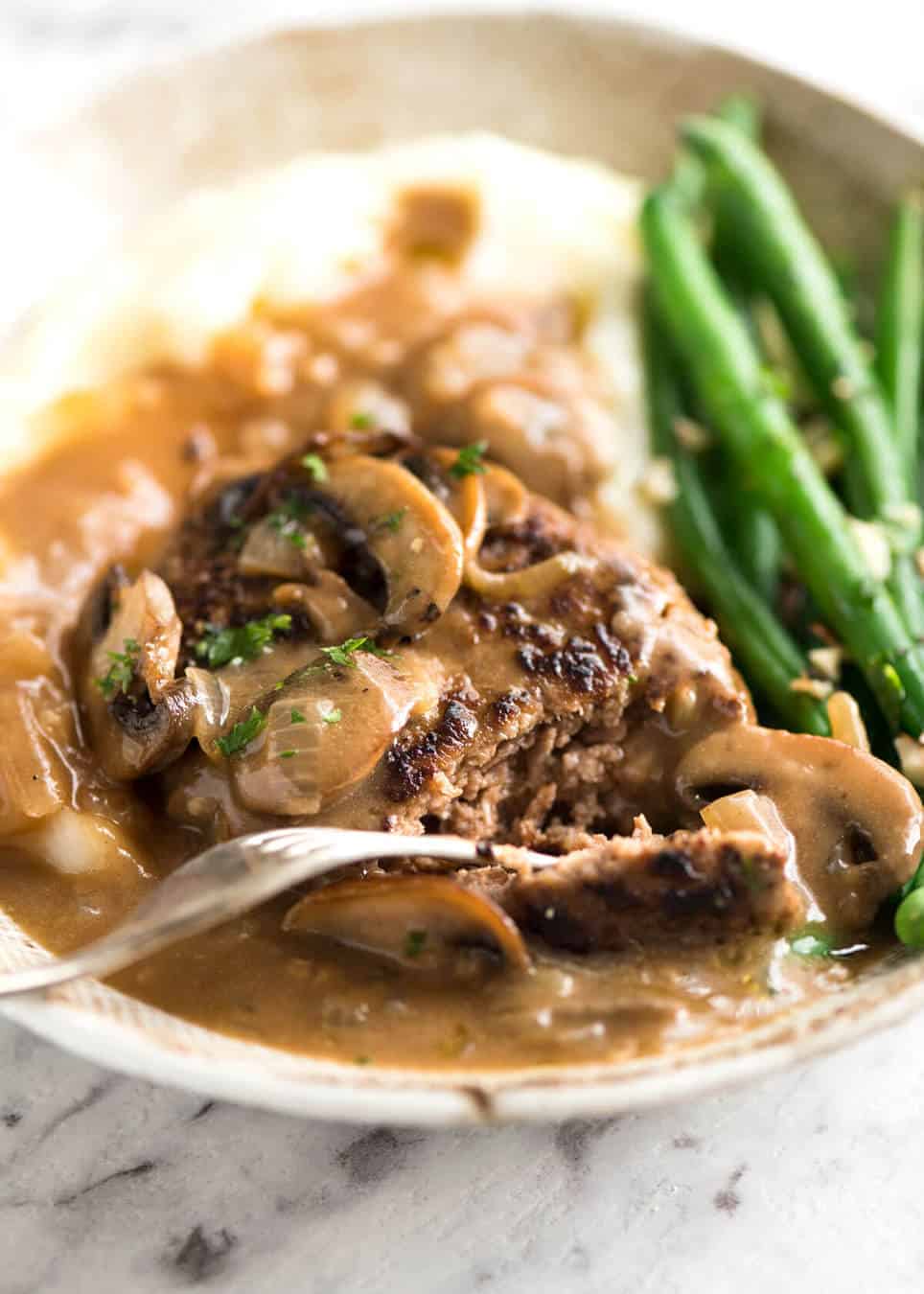 Close up of Salisbury Steak recipe on a plate with mashed potato and green beans.