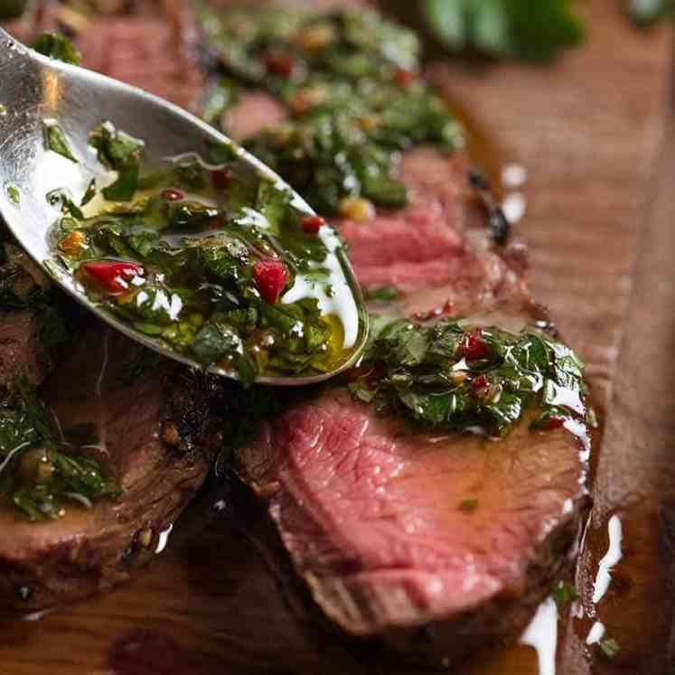 Close up of spoon drizzling Chimuchurri Sauce on steak
